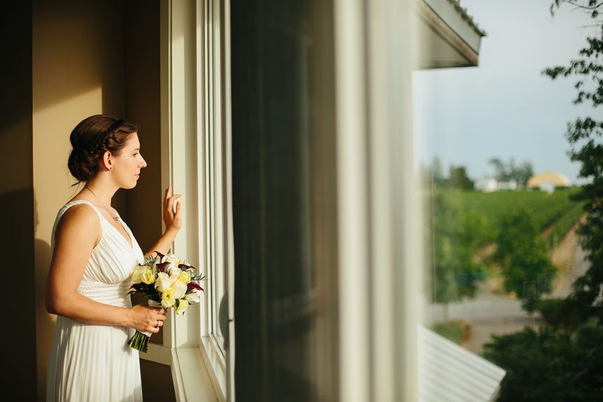 A bride looks through the window before her Flat Rocks Cellars wedding as photographed by Jordan, Ontario wedding photographer.