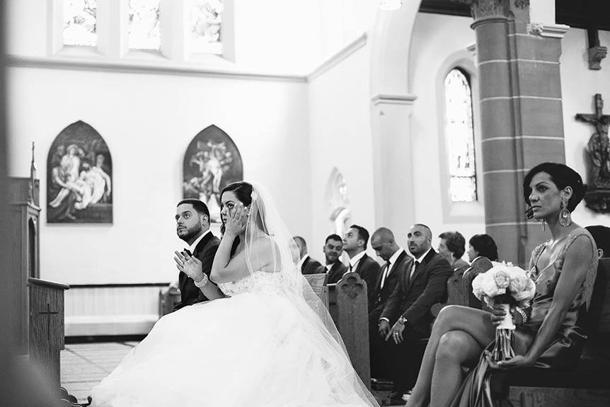 Toronto documentary wedding photographer captures a candid moment where the bride wipes her tears away during her Toronto catholic wedding ceremony.