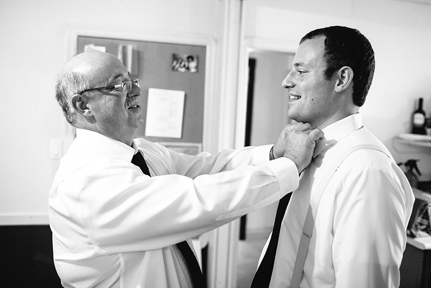 The father of the groom helps his son with his tie.
