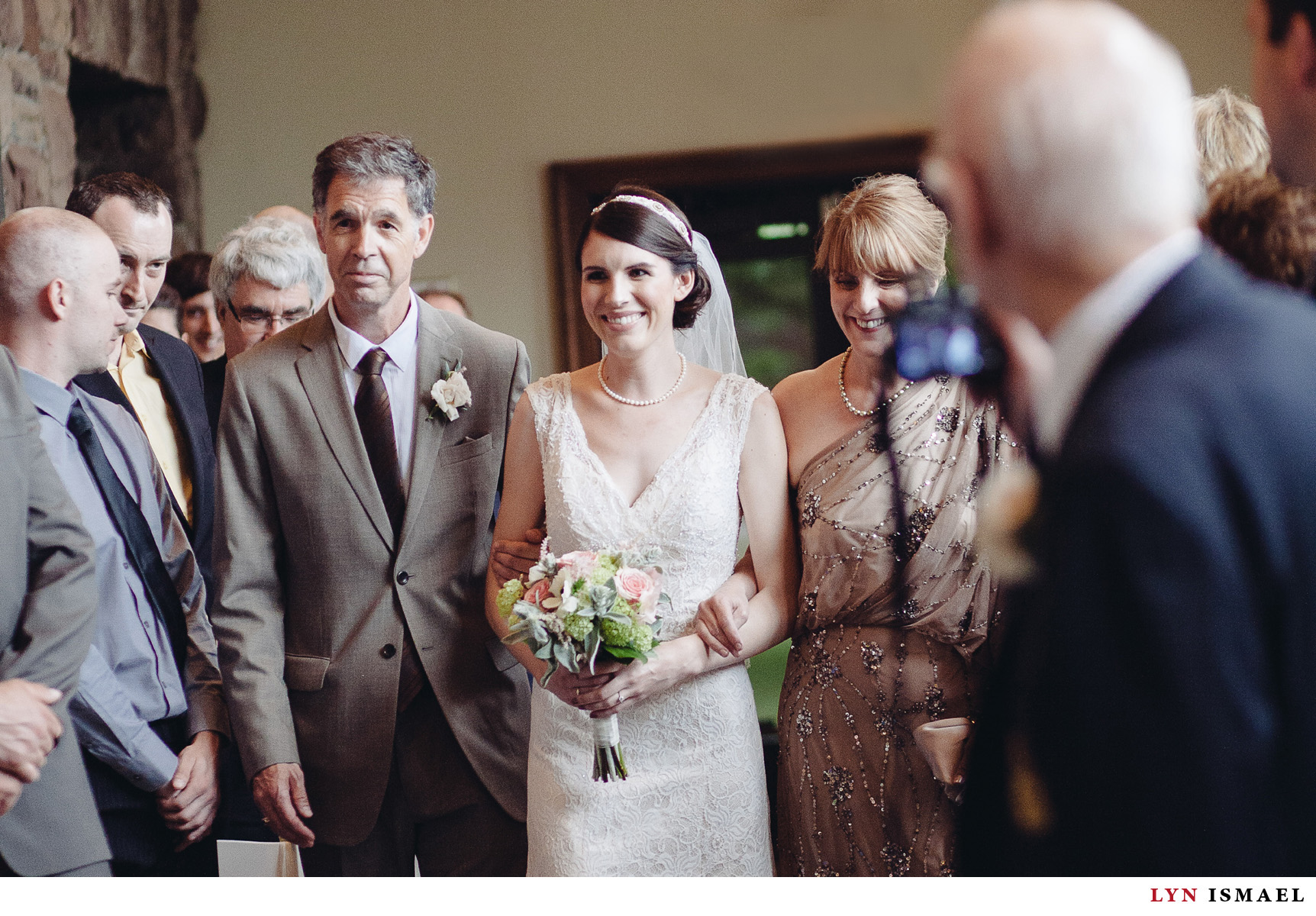 The bride walks down the aisle in Windermere Manor accompanied by her parents.