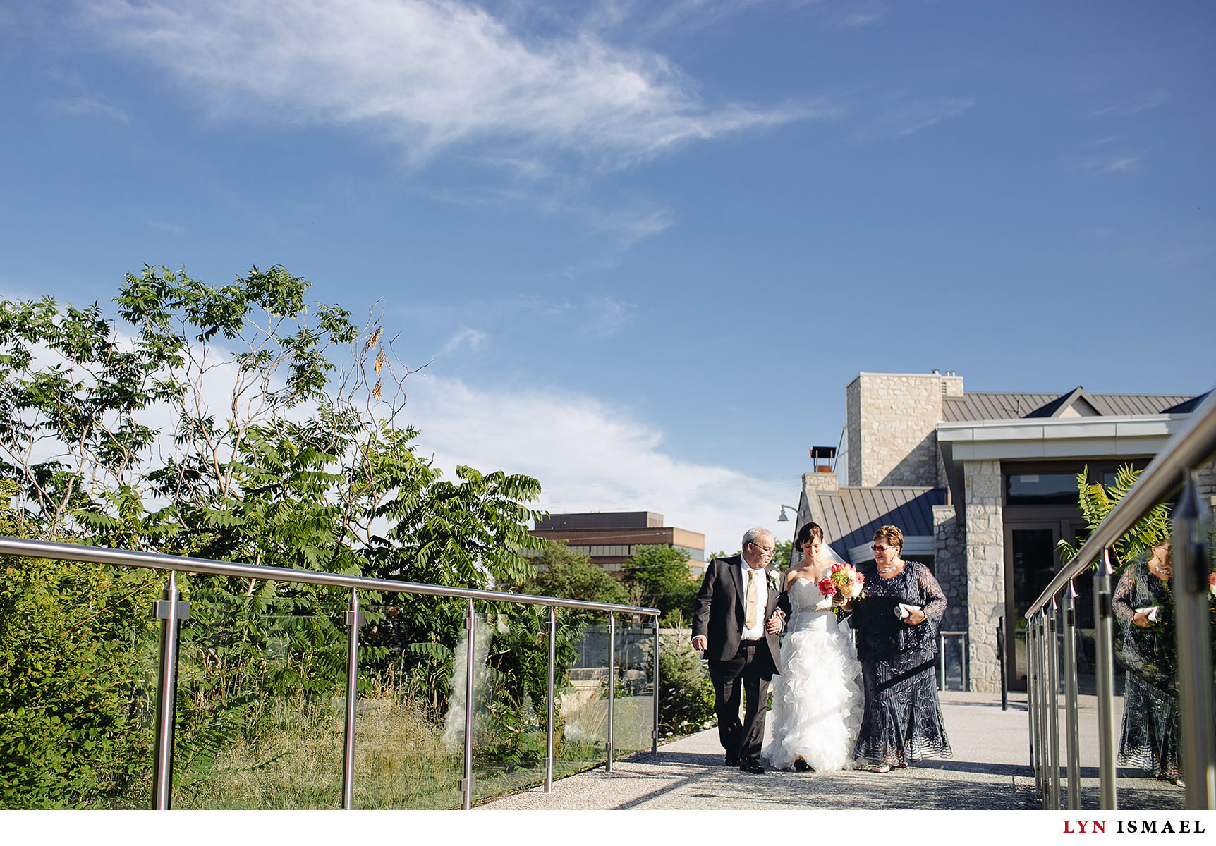 The bride walks down the aisle with her parents at Cambridge Mill.