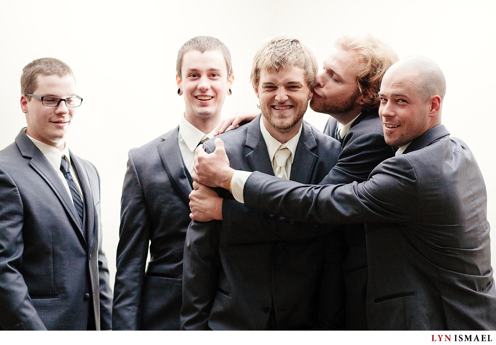 The groomsmen giving the groom a big kiss for the camera.