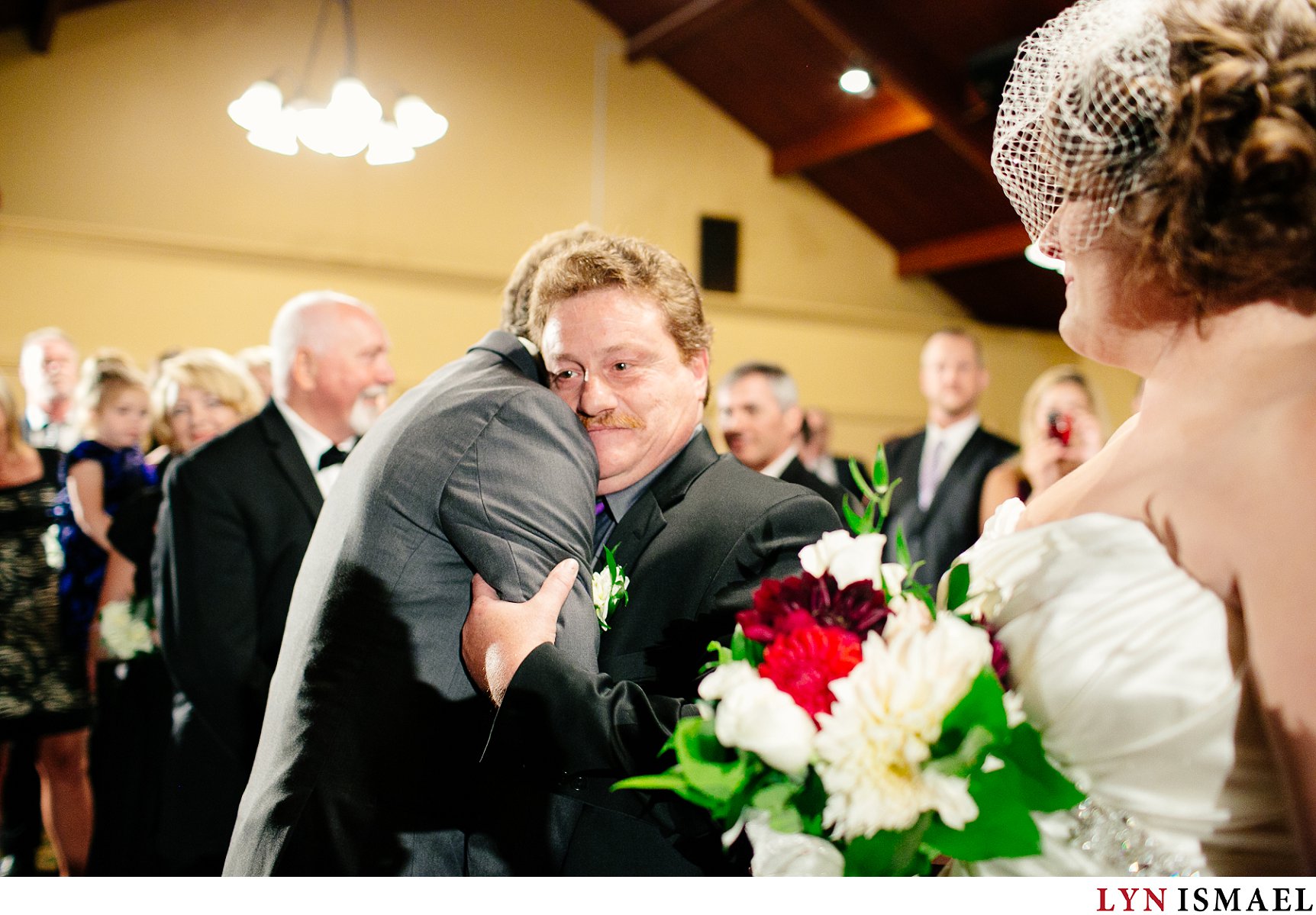Wedding photojournalist captures the father of the bride hugging the groom as he gives his daughter's hand in marriage.