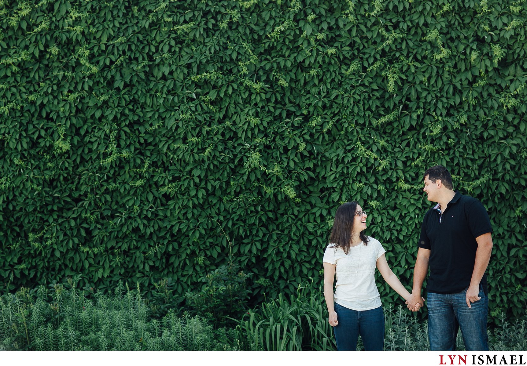 An engaged couple stand in front of a wall of ivy at the parking lot of Ontario Science Centre