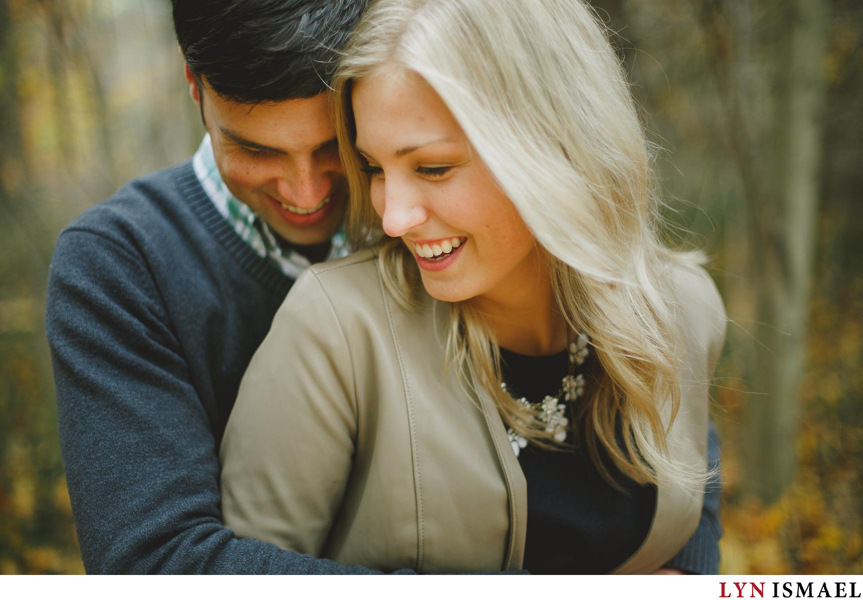A young man hugs his fiancee from behind for their fall engagement photo session