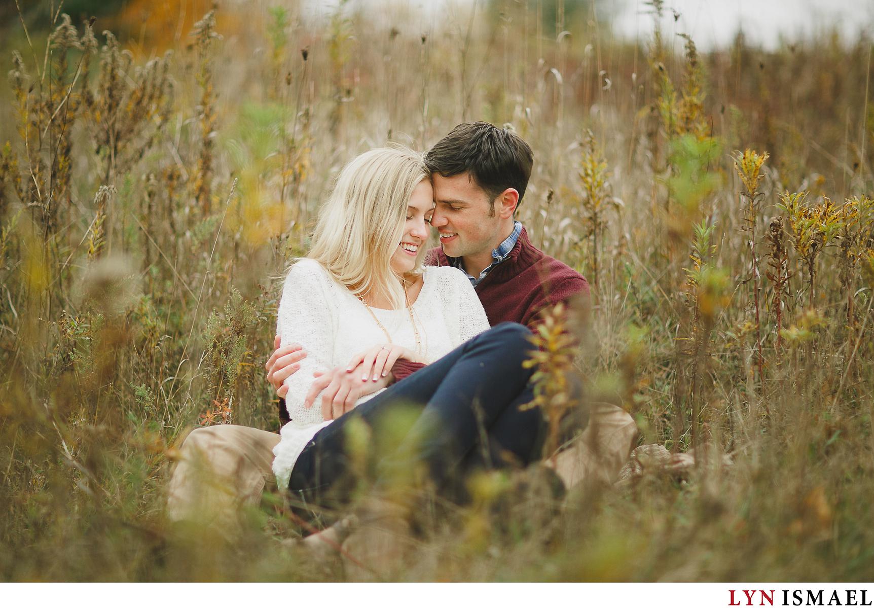 A couple snuggles in the middle of the field for their fall engagement photos