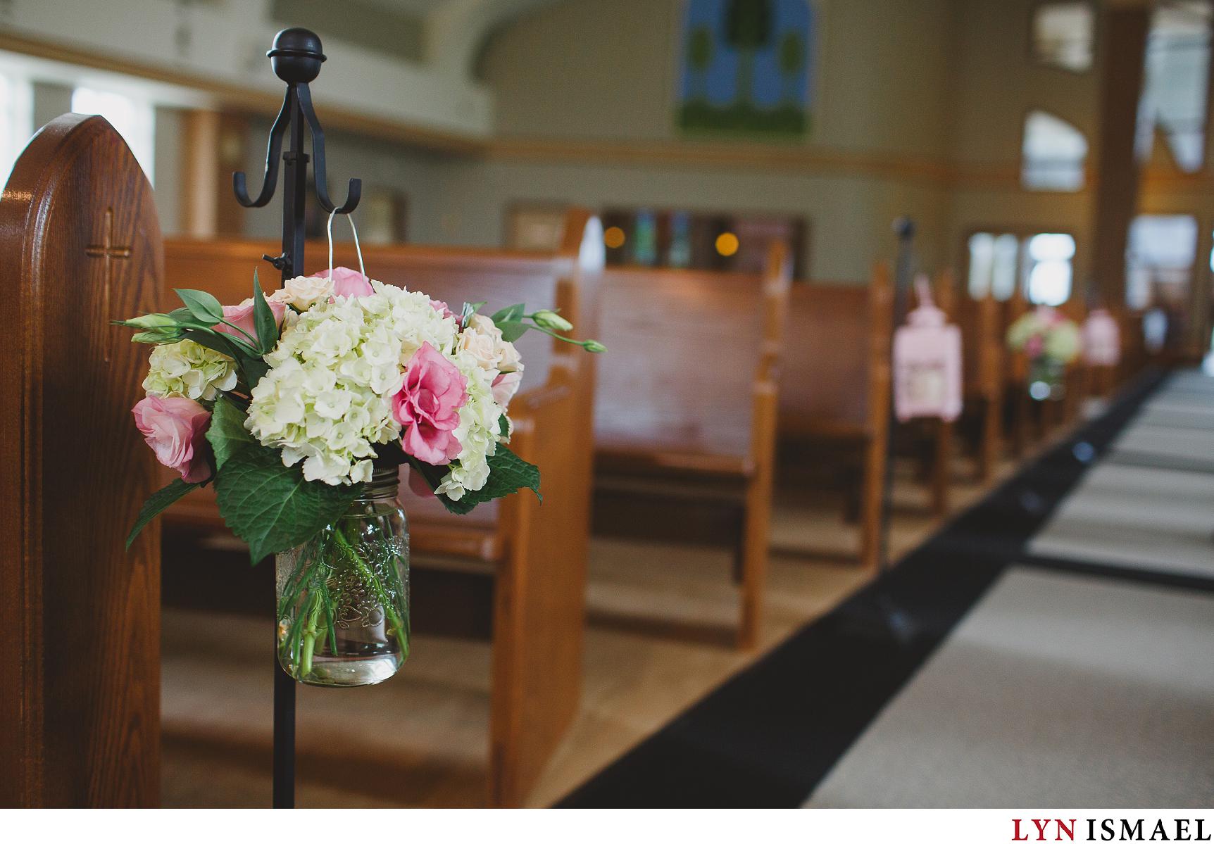 Pink flowers and green hydrangeas decorate the pews at a wedding inside Immaculate Heart Of Mary Roman Catholic Church in Stoney Creek, Ontario.