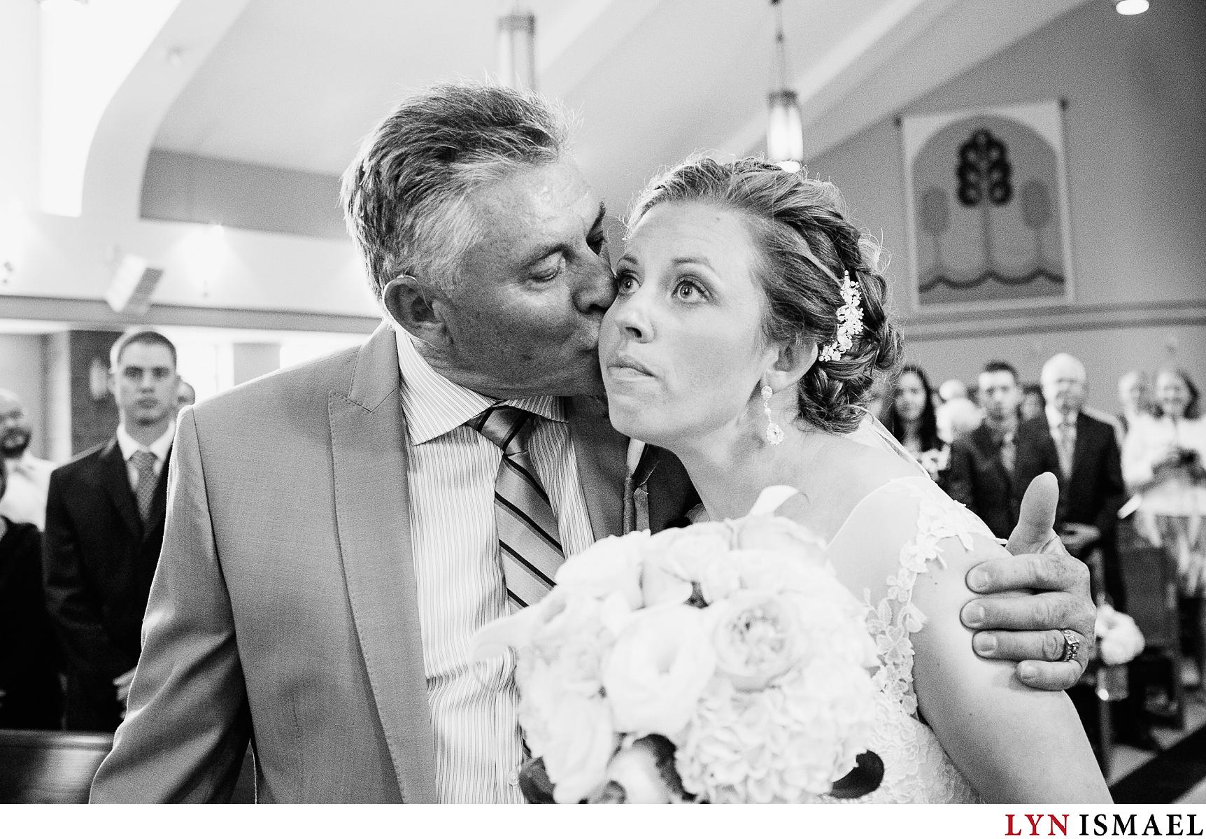 Father of the bride kisses his daughter in the cheeks right before he gives her away.