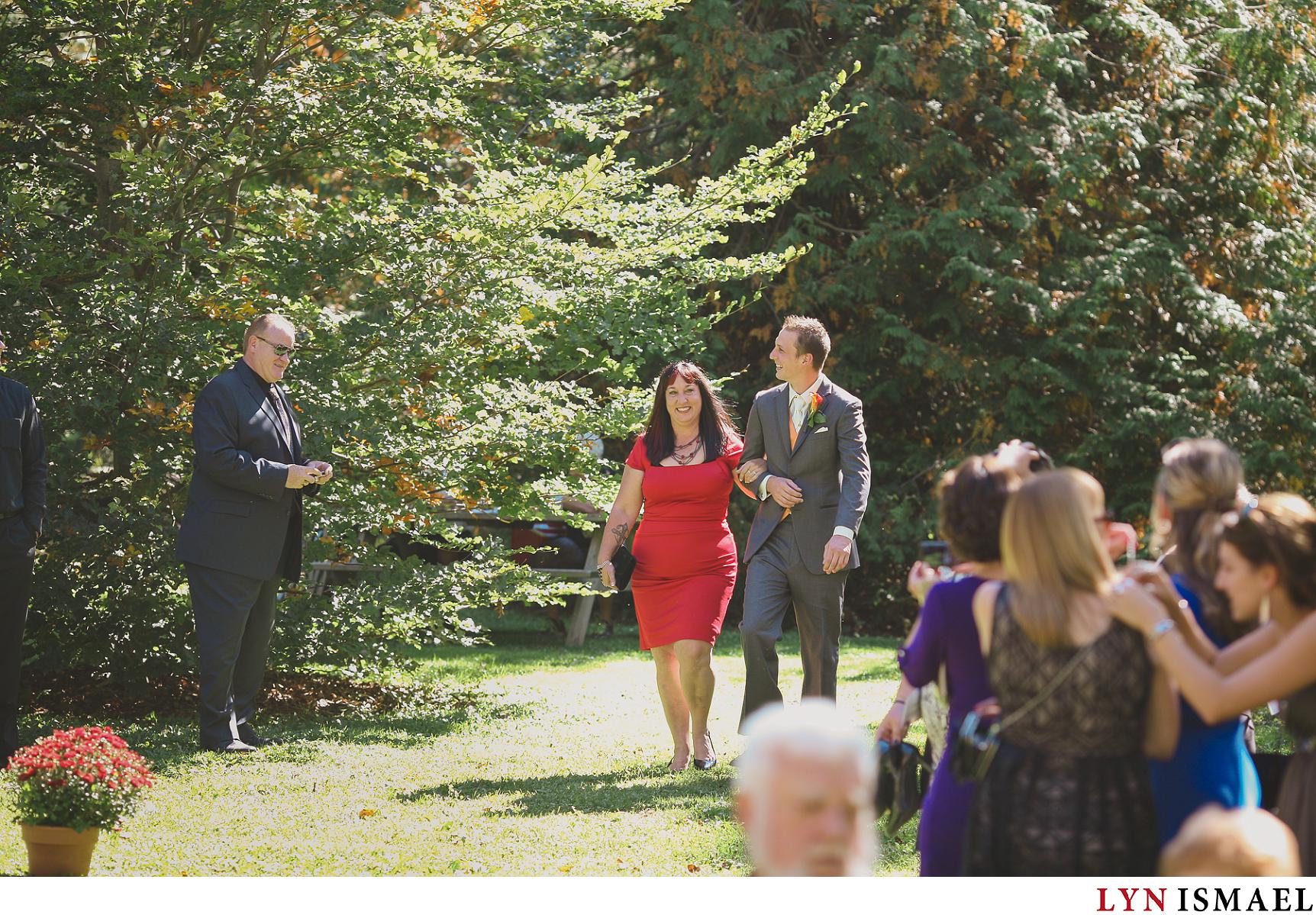 Groom walks down the aisle with his mother at an outdoor wedding ceremony in Elora, Ontario.