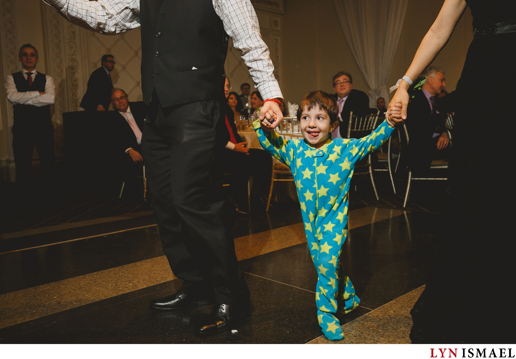 A little boy wearing star print onesie dances with his parents at a wedding reception in Vaughan, Ontario.