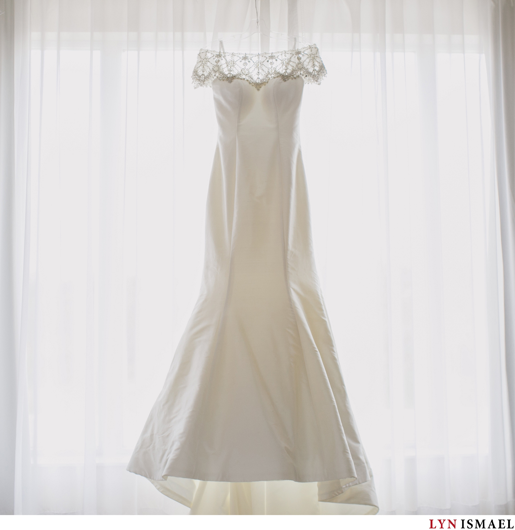 The bride's wedding gown hanging by the window.