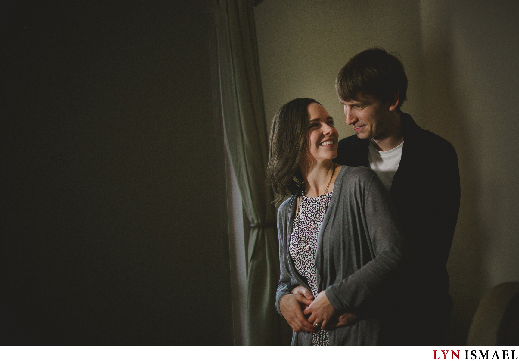 A couple snuggles in their apartment for their engagement session.