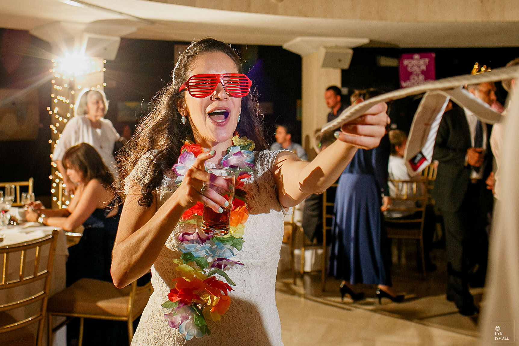 Bride wearing floral leis and red sunglasses grabs her groom on the dance floor with his tie at their Columbus Event Centre wedding.