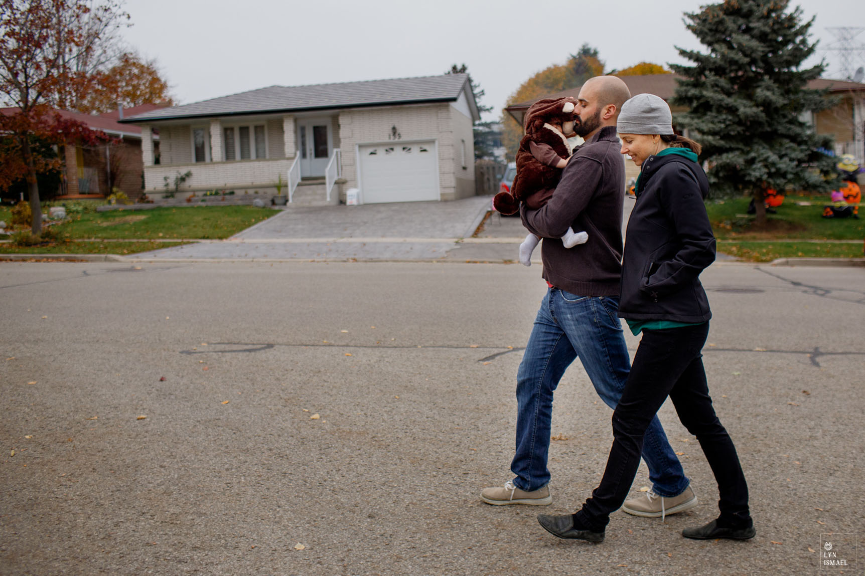 A young couple accompanies their baby at his first trick or treating as documented by Kitchener family documentary photographer.