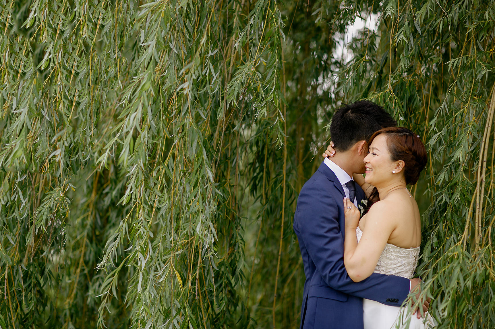 Bride and groom snuggles under a willow tree in Richmond Green Sports Centre