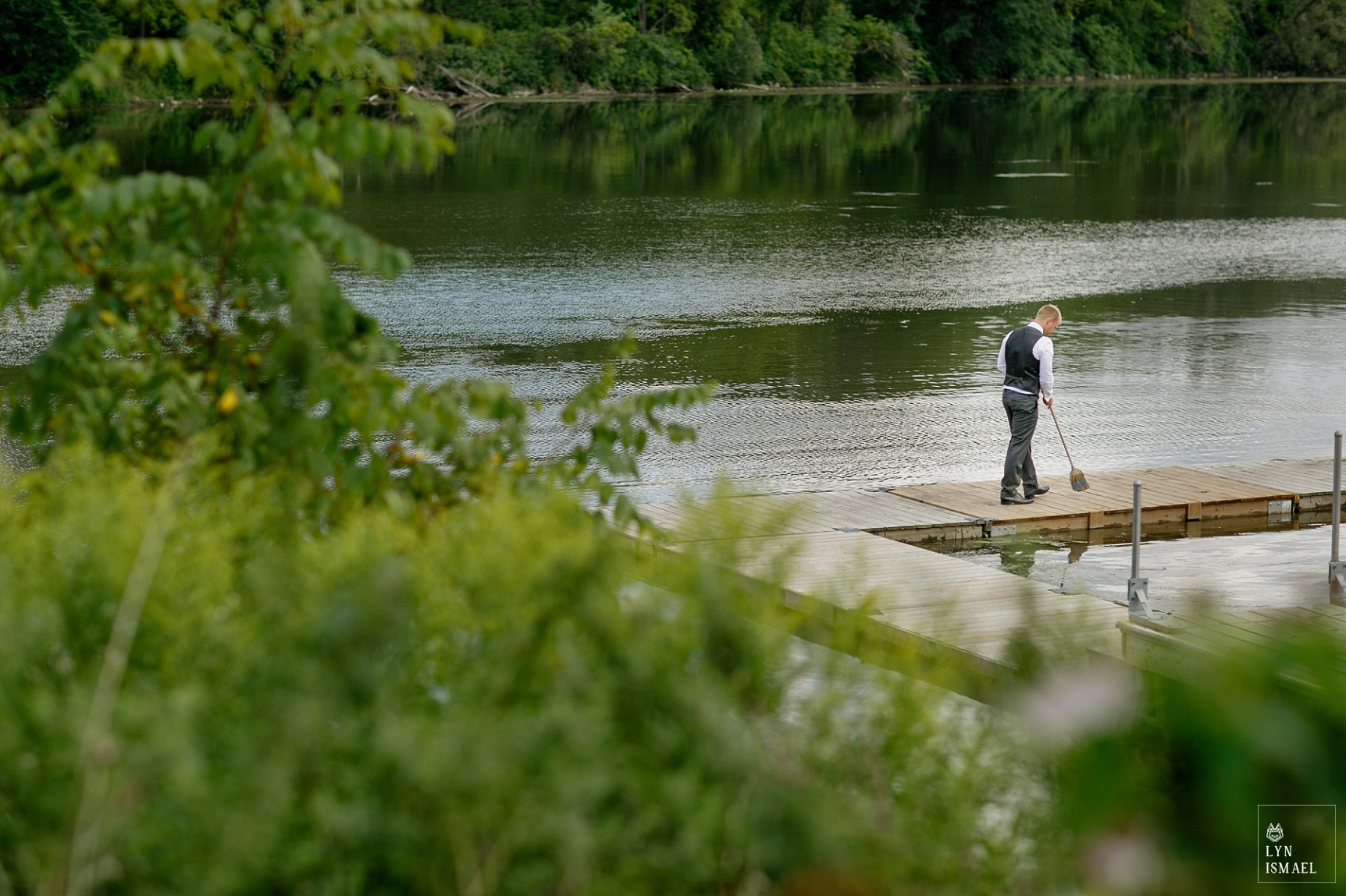 Groomsman cleans the dock of geese droppings before the bride and groom's first look.