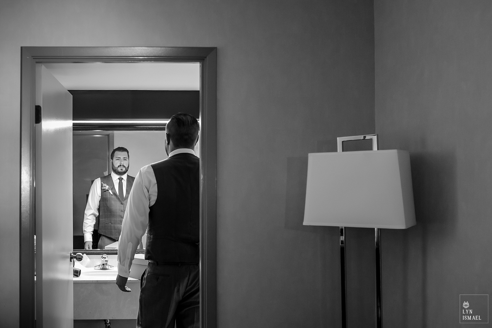 Groom looks at himself in the mirror at his hotel room