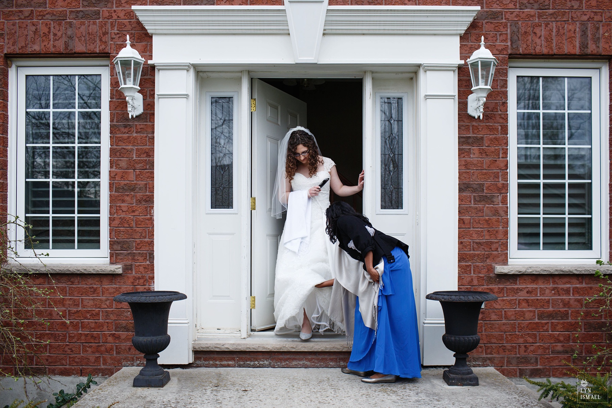 Bride comes out of her parent's house in Wellesley, being helped by her bridesmaid.