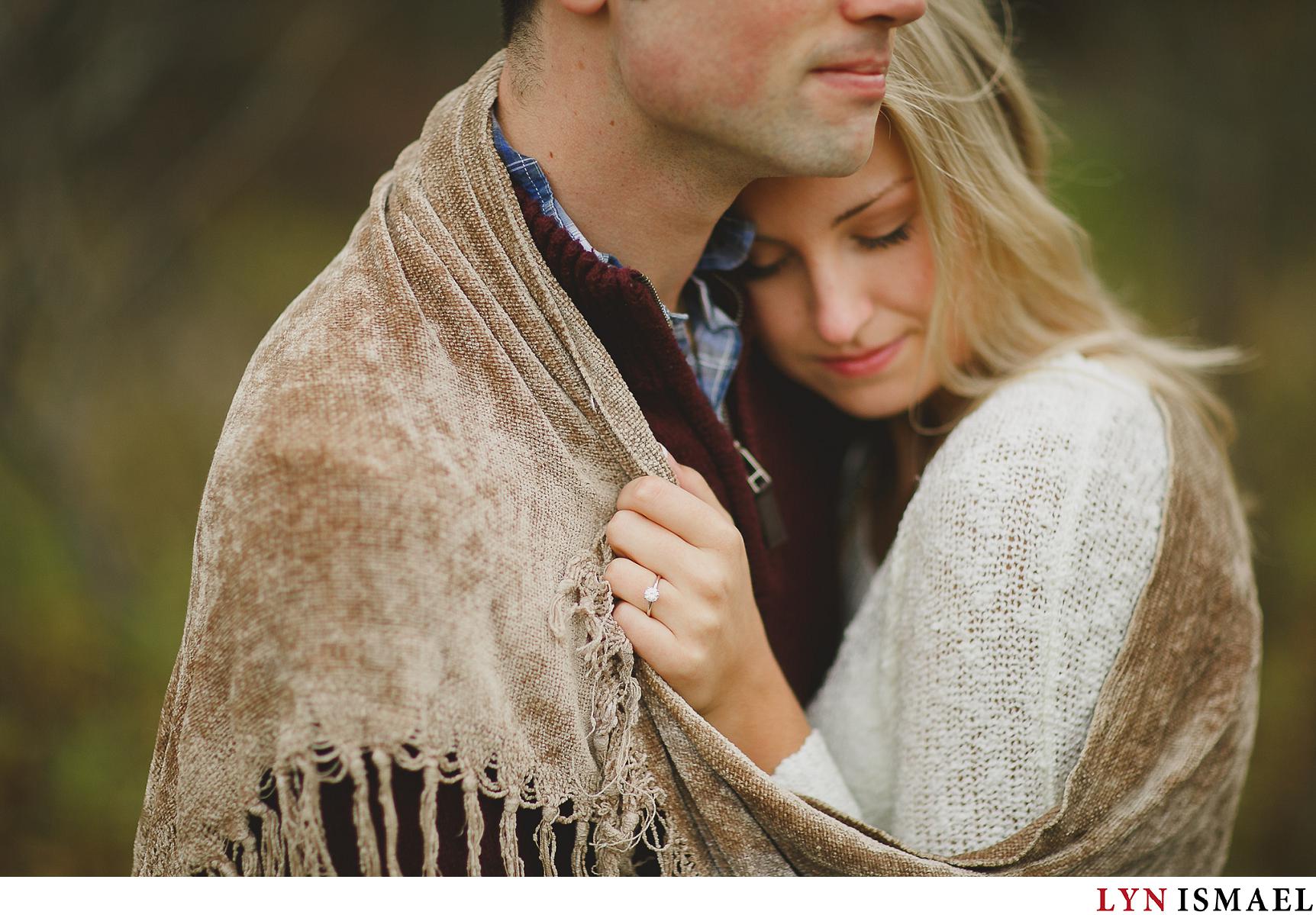 An engaged couple snuggle with a brown blanket for their fall engagement photos